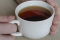 Close-up of male hands and a mug with tea on a beige surface.