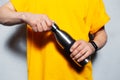 Close-up of male hands opens reusable metal bottle. Young man wearing yellow shirt on the background of white wall.