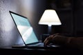 Close-up of male hands typing on keyboard of laptop near table lamp in dark room of house. Royalty Free Stock Photo