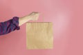 Close up male holding in hand brown clear empty blank craft paper bag for takeaway  on pastel pink background Royalty Free Stock Photo