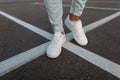 Close-up of male legs. Fashionable young man stands on the asphalt road in leather stylish white sneakers in trendy blue jeans. Royalty Free Stock Photo