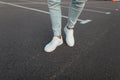 Close-up of male legs. Trendy young fashionable man in vintage blue jeans in leather stylish white sneakers stand on the asphalt Royalty Free Stock Photo