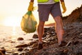 Close up of male legs of volunteer walking on wild coast holding plastic bag full of garbage. Concept of ecological Royalty Free Stock Photo