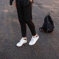 Close-up of male legs. Young fashionable guy in vintage black pants in leather stylish white sneakers posing standing Royalty Free Stock Photo