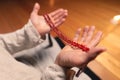 Close-up of a male monk`s hand holding a red wooden rosary in a dark study room. Religion faith