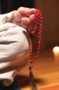 Close-up of a male monk`s hand holding a red wooden rosary in a dark study room. Religion faith