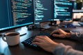 Close up of a male programmer coding at a desk with coffee mug and multiple monitors in office