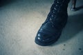 Close-up of a male soldier in black combat boots, leather shoes, standing on a cement floor.