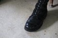 Close-up of a male soldier in black combat boots, leather shoes, standing on a cement floor.