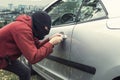 Close up of man in black robber mask breaking the car lock on a city background. Ill-intended thief forces the vehicle