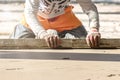 Close up of man builder placing screed rail on the floor covered with sand-cement mix at construction site. Male worker leveling