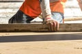 Close up of man builder placing screed rail on the floor covered with sand-cement mix at construction site. Male worker leveling