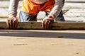 Close up of man builder placing screed rail on the floor covered with sand-cement mix at construction site. Male worker leveling