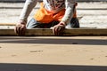 Close up of man builder placing screed rail on the floor covered with sand-cement mix at construction site. Male worker leveling