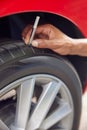 Close-Up Of Man Checking Tread On Car Tyre With Gauge