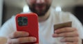 Close up of man client sitting on the couch holding banking credit card and smartphone using mobile payments in the Royalty Free Stock Photo