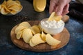 Close-up of a man dips potato chips into sauce in a white bowl on a wooden cutting board Royalty Free Stock Photo