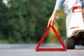 Close up of man driver putting red warning triangle/emergency stop sign behind his broken car Royalty Free Stock Photo