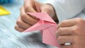 Close up man folding pink origami frog.