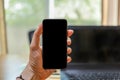 Close up of man hand holding mobile smartphone with blank screen copy space and computer laptop in office Royalty Free Stock Photo