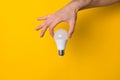 Close up man hand holding white led light bulb against yellow background. concept of creativity, inspiration and new Royalty Free Stock Photo