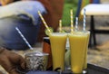 Man hand tray with glasses of passion fruit and mango juices as colorsof straws and fresh fruits on table