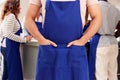 Close Up Of Man With Hands In Apron Pocket Taking Part In Cookery Class In Kitchen