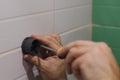 Close-up of man hands attaching plastic component of shower head holder to tiled wall screwing in nail with screwdriver Royalty Free Stock Photo