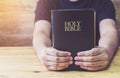 Close up of a man hands hold the holy bible on wooden table with window light