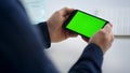 Close up man hands holding smartphone with green screen. Male looking cell phone