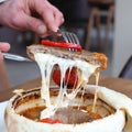 Close-up of a man holding a fork, pulling out a slice of meat topped with melting mozzarella cheese