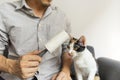 Man holding lint roller sitting on a sofa with a cute cat sit beside. Royalty Free Stock Photo
