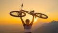 CLOSE UP Man lifts his bicycle above head at sunset after a mountain biking trip Royalty Free Stock Photo