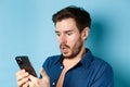 Close-up of man looking shocked and reading message on smartphone, gasping and stare startled at screen, standing on