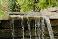 Close up of a man made stone waterfall with trees in the background during the summer