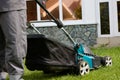 Close-up of a man in overalls with a lawn mower cutting grass in a modern garden Royalty Free Stock Photo