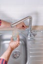 Man pouring glass of water from tap with clean filter in kitchen, close up