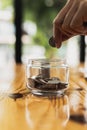 Close-up of a man putting a coin in a glass jar with a bunch of coins inside, he is a stock fund investor and stock investor.