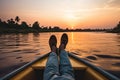 Close up of man\'s feet in boat on the river at sunset, Crop unrecognizable barefooted male traveler sitting on edge of boat