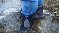 Close-up of man`s feet in high boots step on ice and fall into puddle