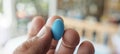 Close up of a man s hand holding a blue pill with blurred bedroom background, space for text Royalty Free Stock Photo