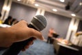 Close up of man`s hand holding microphone in conference hall or meeting event with blurred background Royalty Free Stock Photo