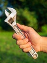 Close-up of a man`s hand holding an old adjustable wrench. Blurry green background. The concept of a tool for work. Vertical phot Royalty Free Stock Photo