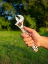 Close-up of a man`s hand holding an old adjustable wrench. Blurry green background. The concept of a tool for work. Vertical phot Royalty Free Stock Photo