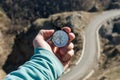 Close-up A man`s hand holds a pocket compass against the backdrop of a mountain road and forest. The concept of outdoor