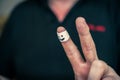 Close-up of a man`s hand showing a gesture of victory. White armband on adult male index finger. Smiling face painted on the