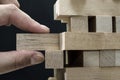 Close up of man`s hand take one block to a tower of wooden blocks, dark tone. Royalty Free Stock Photo