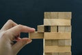 Close up of man`s hand take one block to a tower of wooden blocks, dark tone. Royalty Free Stock Photo