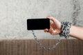 Close-up, the man`s hand is tied with a chain to the smartphone. The concept is dependent on technology, phone, social networks,