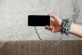 Close-up, the man`s hand is tied with a chain to the smartphone. The concept is dependent on technology, phone, social networks,